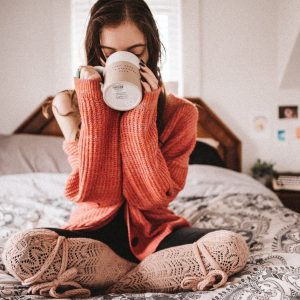 woman in red knit sweater holding white ceramic mug